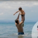 screenshot with man throwing child in the air at the beach in sea